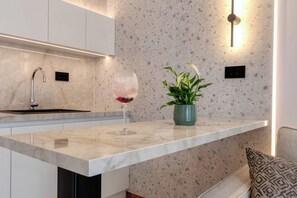 A modern kitchen with a marble countertop, a wine glass, a potted plant, and a built-in light fixture. - Lemar (Hersonissos)