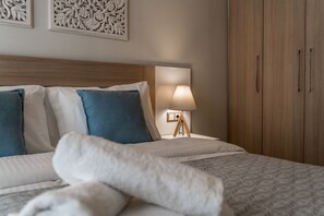 A neatly made bed with white and blue pillows, a bedside lamp, and a wooden wardrobe. - Lemar (Hersonissos)