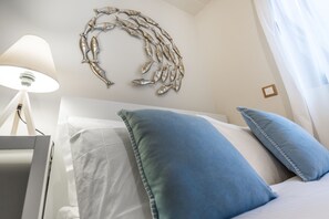 A neatly made bed with blue pillows, a wall-mounted fish decoration, and a lamp on a bedside table. - Lemar (Hersonissos)