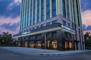 A modern hotel with a prominent glass facade, multiple entry points, and a well-lit entrance area. - Orange Crystal Hotel Suzhou East Railway Station (Suzhou)