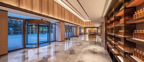A modern hotel lobby with a polished floor, wooden paneling, glass doors, and shelves with bottles.