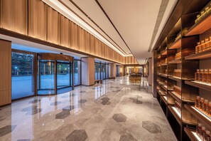 Un moderno vestíbulo de hotel con suelo pulido, paneles de madera, puertas de vidrio y estanterías con botellas.