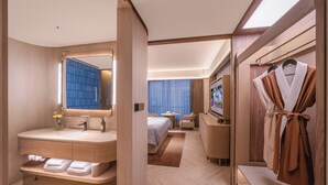 A modern hotel room with a large mirror, a vanity with a sink, a bed with a blue curtain, a TV, and a robe rack. - Orange Crystal Hotel Suzhou East Railway Station (Suzhou)
