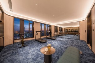 Habitación de hotel con vista a la ciudad, equipo de ejercicio, una mesita con un florero y un sofá.