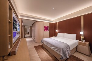 Habitación de hotel moderna con una cama grande, una mesita de noche con lámpara, televisor integrado y un armario de madera.