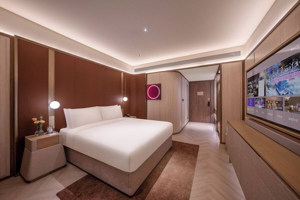 Una habitación de hotel moderna con una cama grande, mesitas de noche, televisión y televisor montado en la pared.