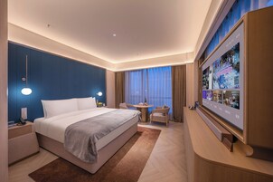 Un hotel moderno con una cama grande, mesitas de noche, un televisor, una pequeña mesa con sillas y vistas a la ciudad.