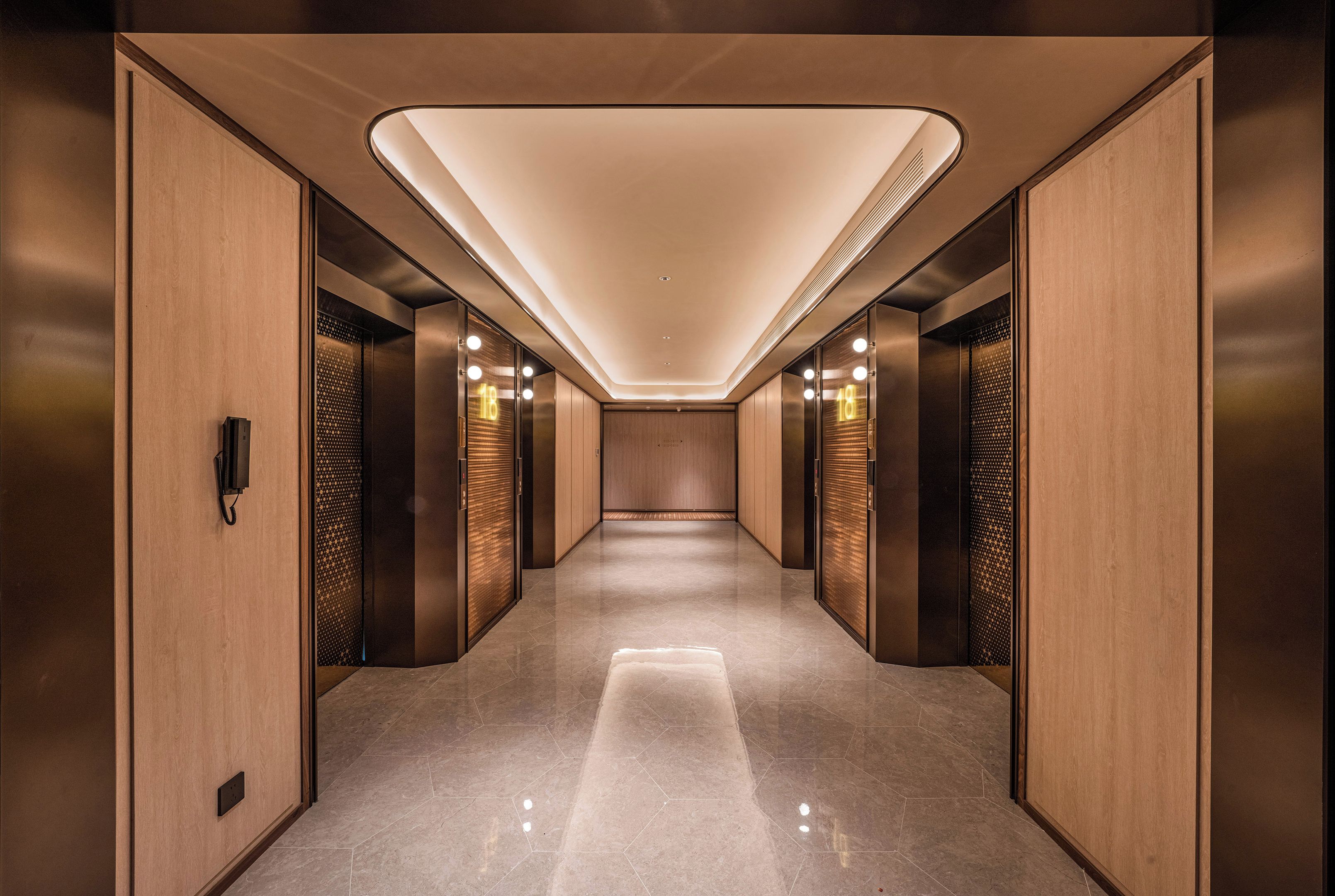 Un hall de ascensores moderno con suelo pulido, paneles de madera e iluminación en el techo.
