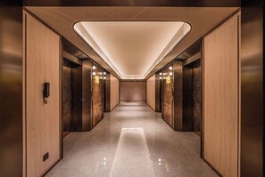 A modern elevator lobby with a polished floor, wooden paneling, and illuminated ceiling lights. - Orange Crystal Hotel Suzhou East Railway Station (Suzhou)