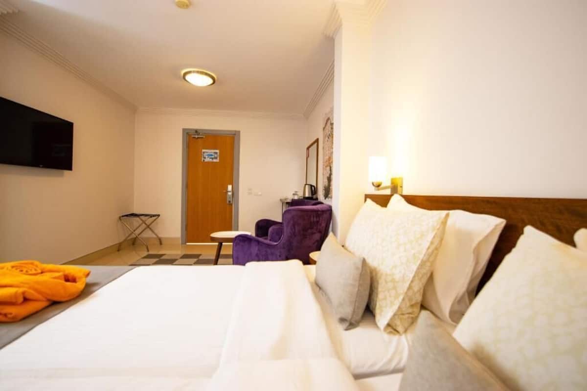 Ein Hotelzimmer mit Bett, Wandfernseher, Tür und kleinem Tisch mit Stuhl.