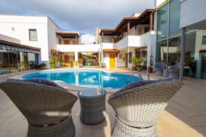 Una piscina con sillas de mimbre, un porche cubierto y un edificio con balcones.
