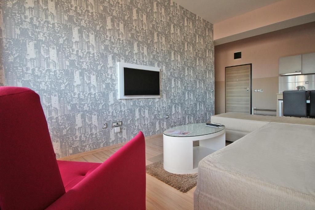 Een moderne woonkamer met een rode fauteuil, een glazen salontafel en behangpapier met een stadsgezicht.
