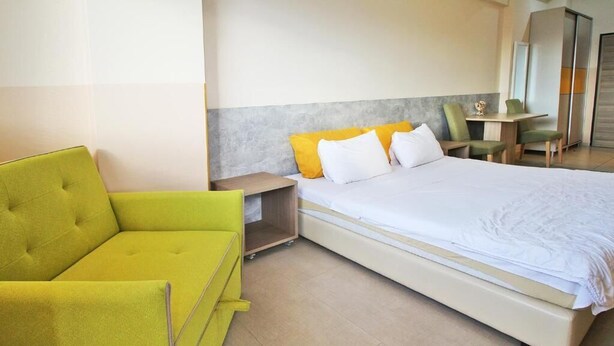 Una habitación de hotel con una cama, un sofá verde, una mesita de noche y una silla.