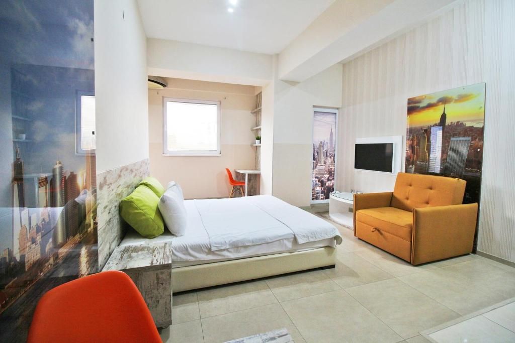 A hotel room with a bed, a chair, a desk, and a cityscape painting on the wall.