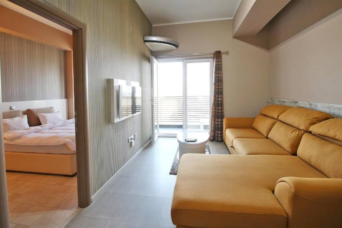 Una habitación de hotel con cama, sofá, televisor y balcón con cortinas.