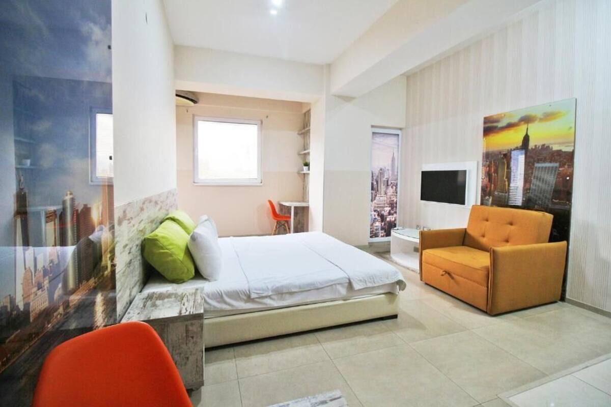 Habitación de hotel con cama, una silla, un escritorio y un cuadro de un paisaje urbano en la pared.