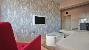 Una sala moderna con una butaca roja, una mesa de centro de vidrio y un papel tapiz con un paisaje urbano.