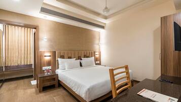 Quarto de hotel com cama, mesas de cabeceira, escrivaninha e televisão.