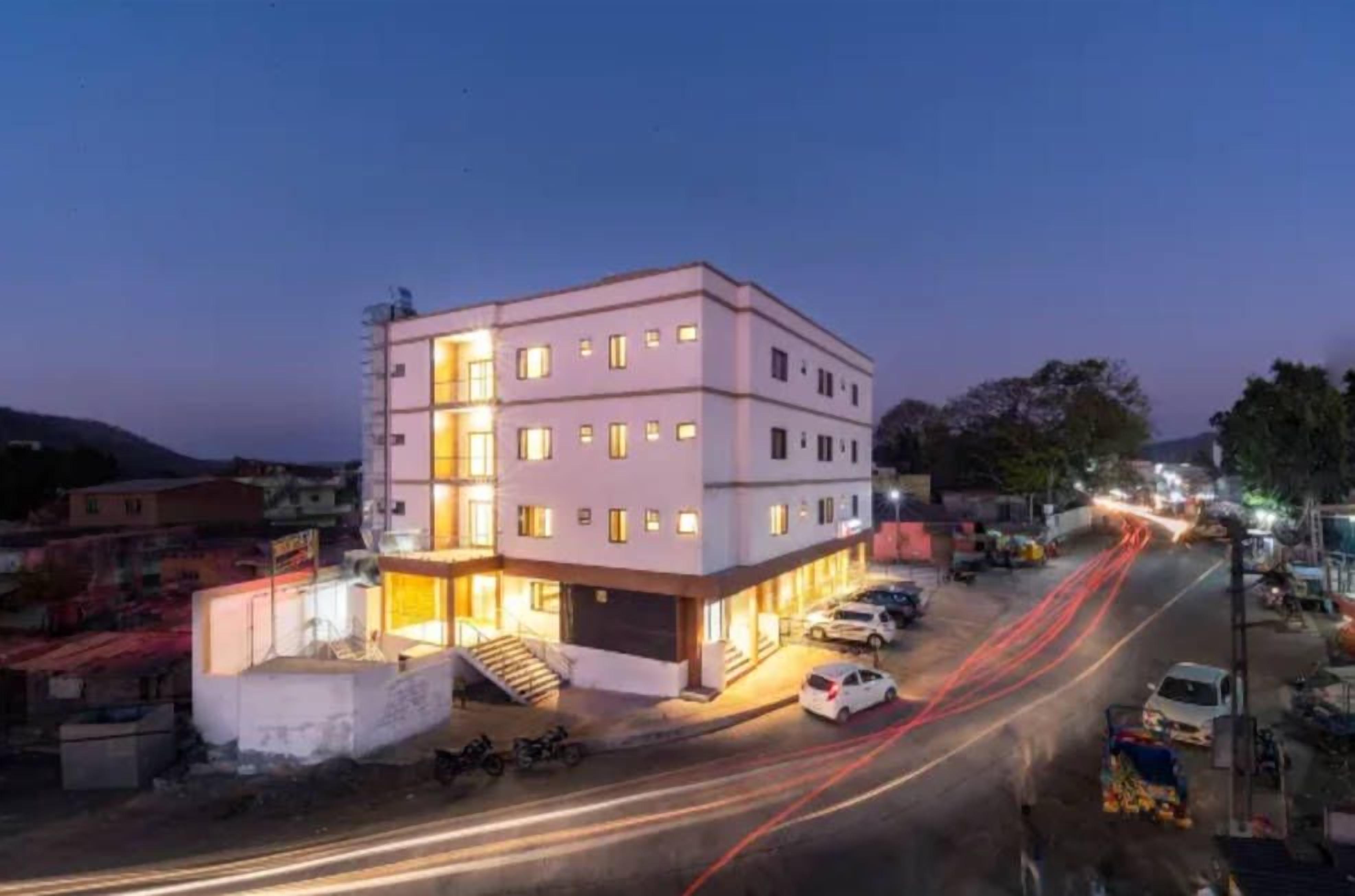 Un hotel de varios pisos con un diseño moderno, que cuenta con una escalera central, múltiples ventanas y un área de estacionamiento.