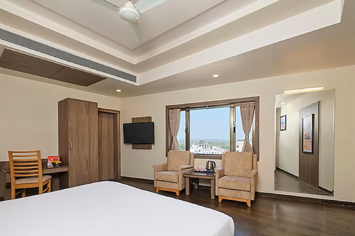 Habitación de hotel con cama, dos sillones, una mesita, televisor y un ventanal con vista a la ciudad.