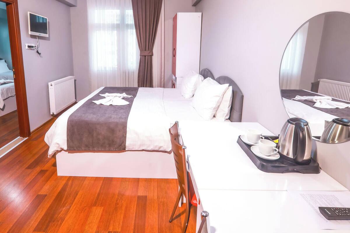 Ein Hotelzimmer mit Bett, Schreibtisch, Stuhl, Spiegel, Fernseher und Heizkörper.