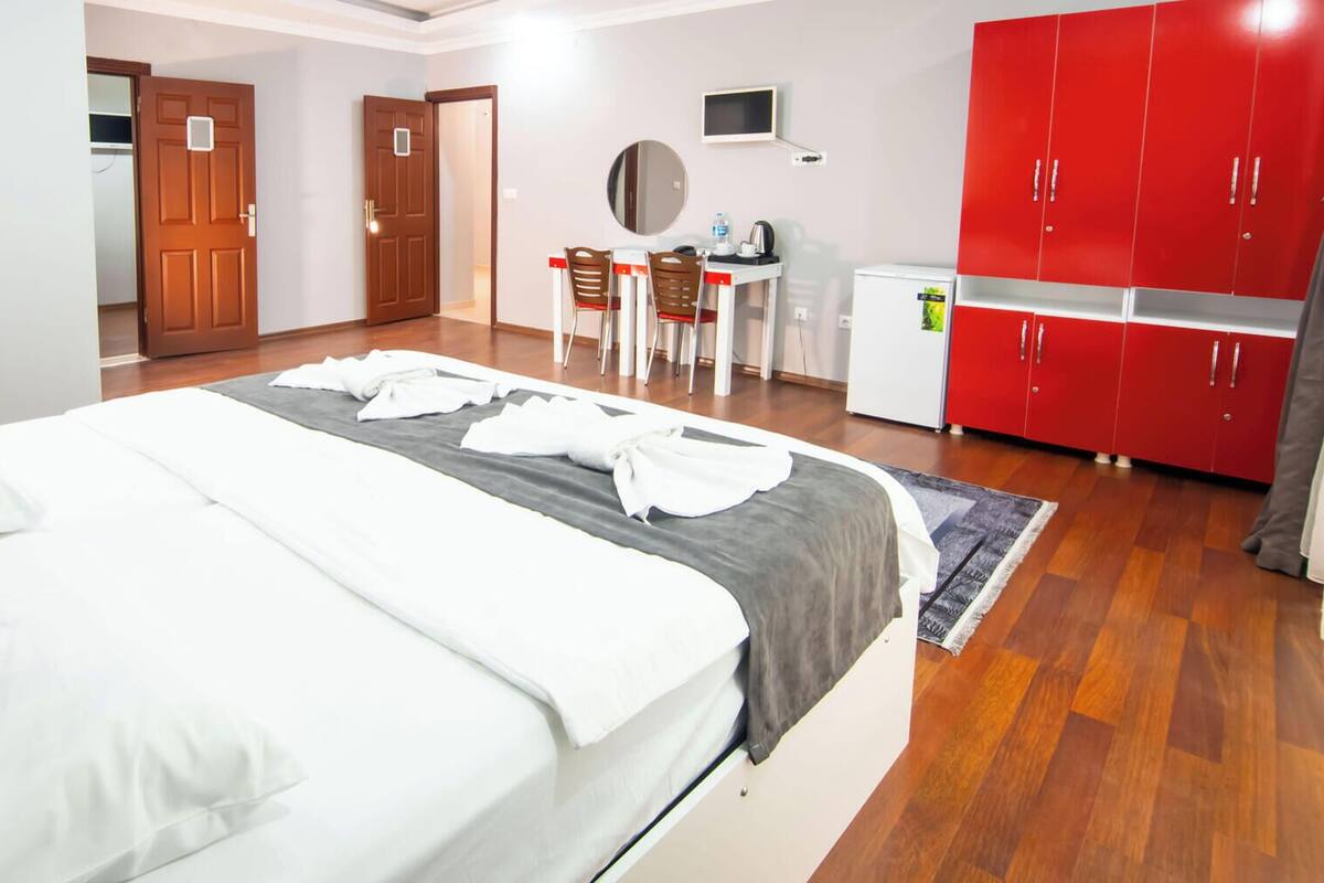 Ein Hotelzimmer mit einem Bett, einem Schreibtisch, einem roten Kleiderschrank und einer kleinen Küchenzeile.