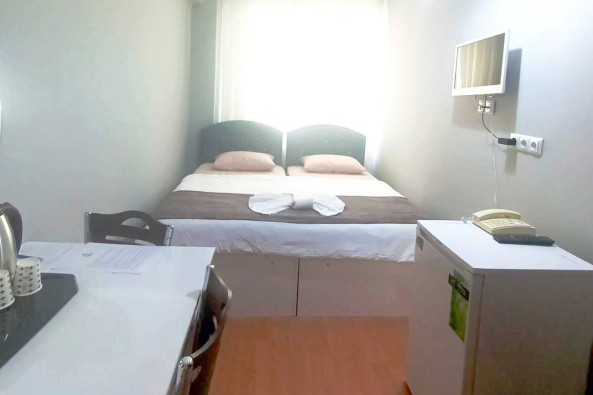 Ein kleines Hotelzimmer mit einem Bett, einem Schreibtisch, einem Stuhl, einem Fernseher und einem Fenster.