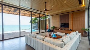 A modern living room with a large sofa, a flat-screen TV, and a view of the ocean. - Sinae Residence Pool Villa (Ratsada)