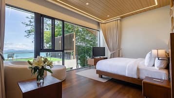 A modern bedroom with a large bed, a TV, a desk, and a view of the outdoors.