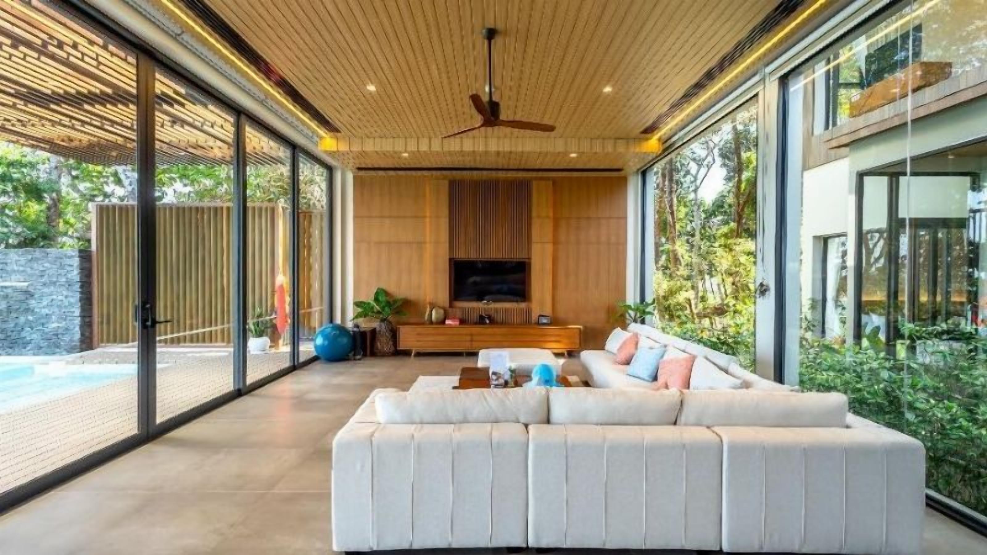 A modern living room with a large sofa, a television, and a ceiling fan.