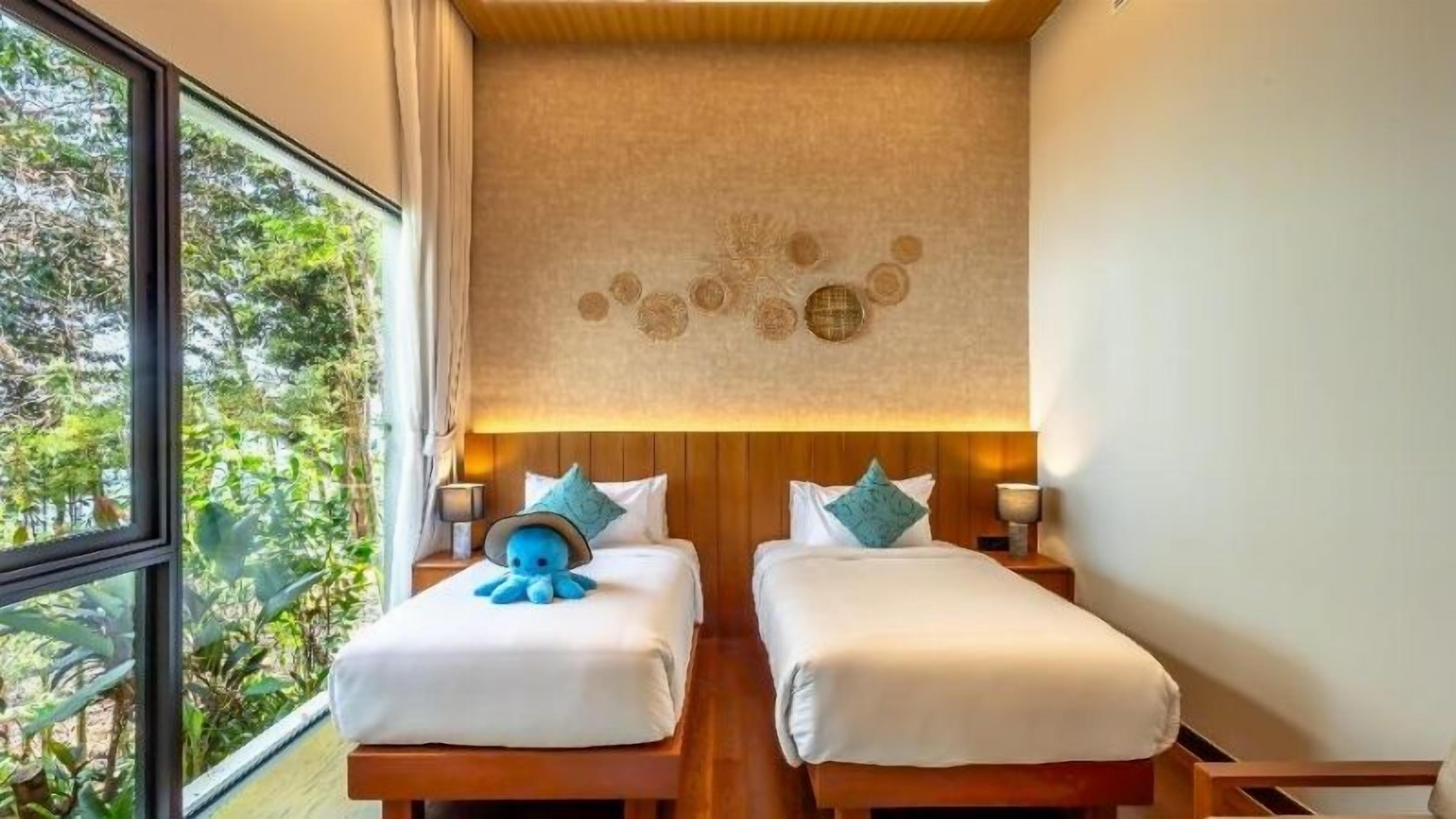 A room with two beds, a wooden headboard, a wall with circular decorations, and a view of greenery outside.