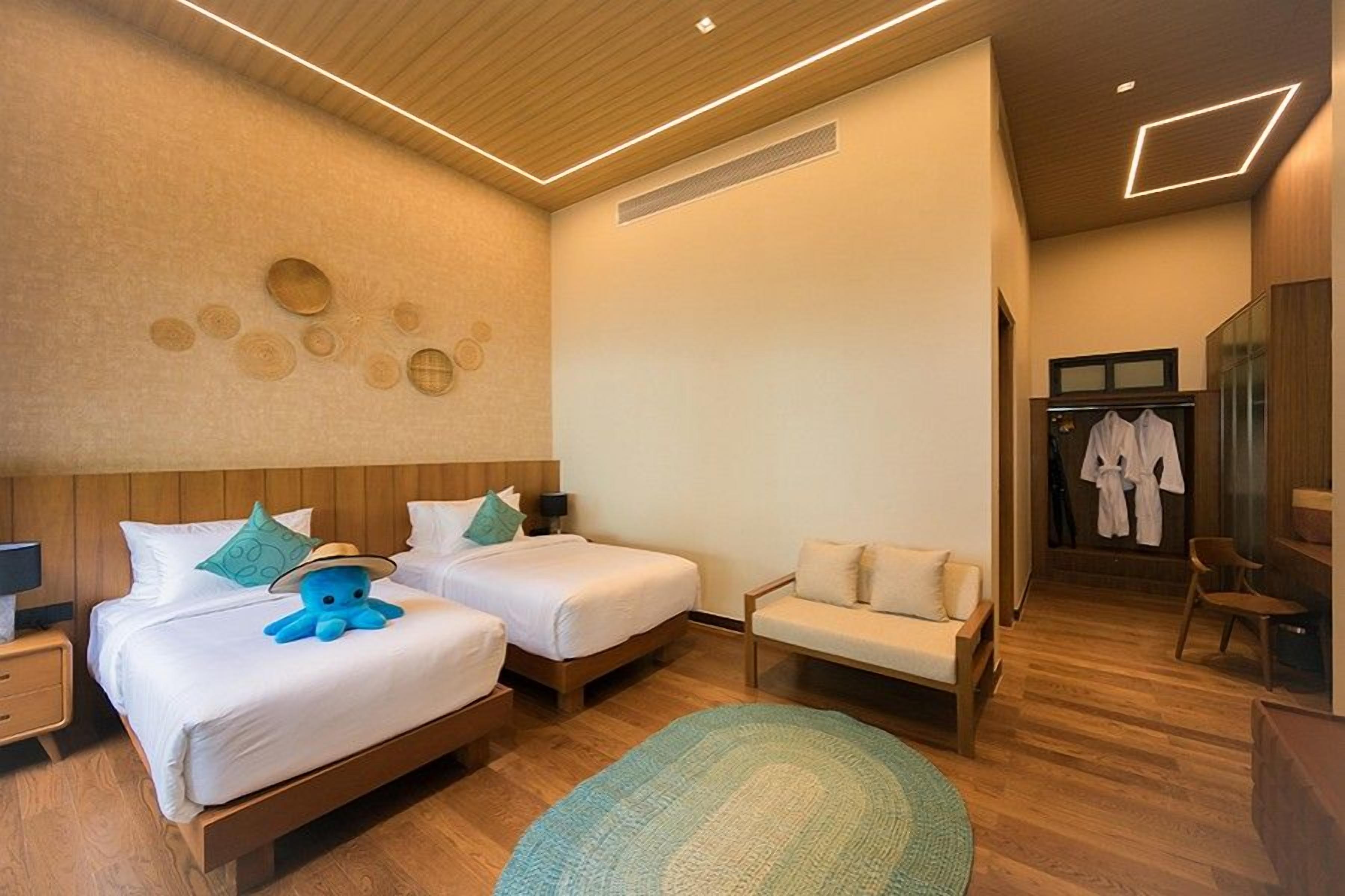 Quarto de hotel com duas camas, um sofá, uma mesa pequena e um espelho.
