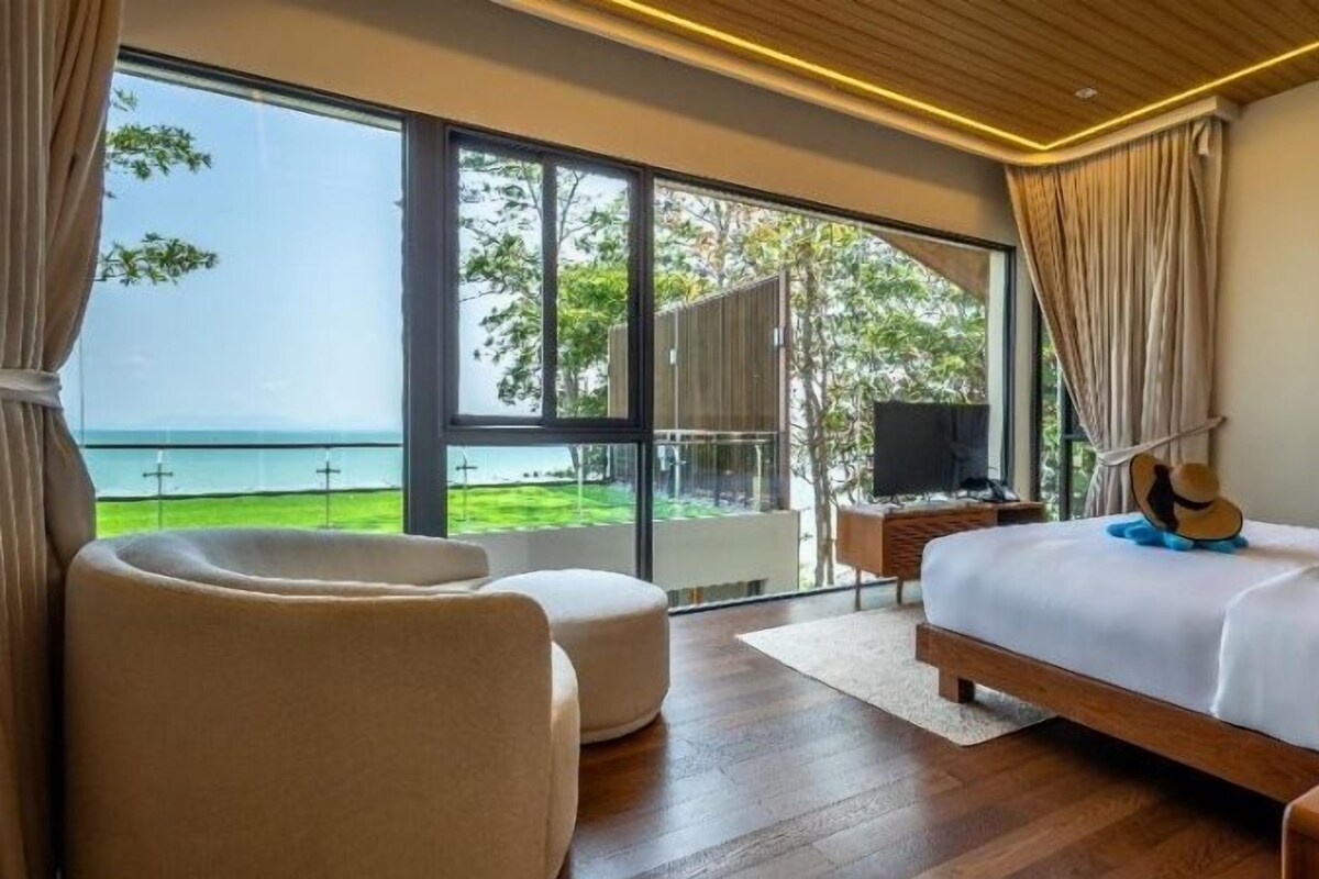 Un dormitorio con una ventana grande, una cama, una silla, una guitarra y un televisor.