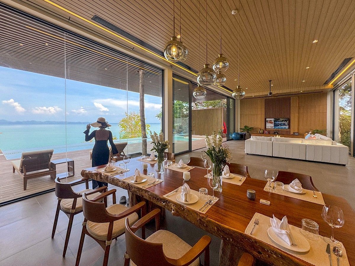 A dining area with a view of the sea, a large wooden table set for a meal, and a modern interior design.
