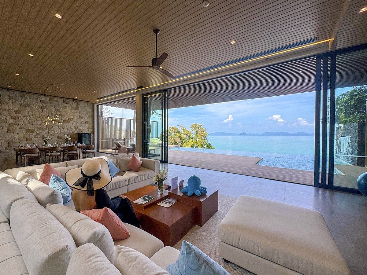 A modern living room with a large sofa, a coffee table, and a view of the sea.