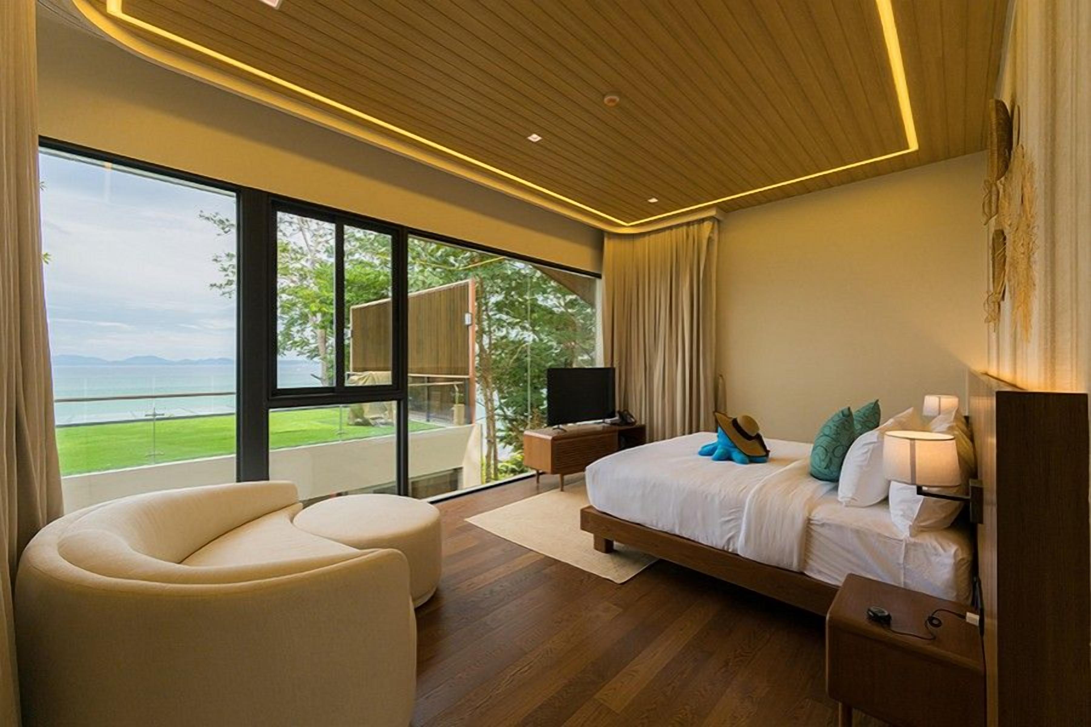 A modern bedroom with a large bed, a sofa, a TV, and a balcony with a view.
