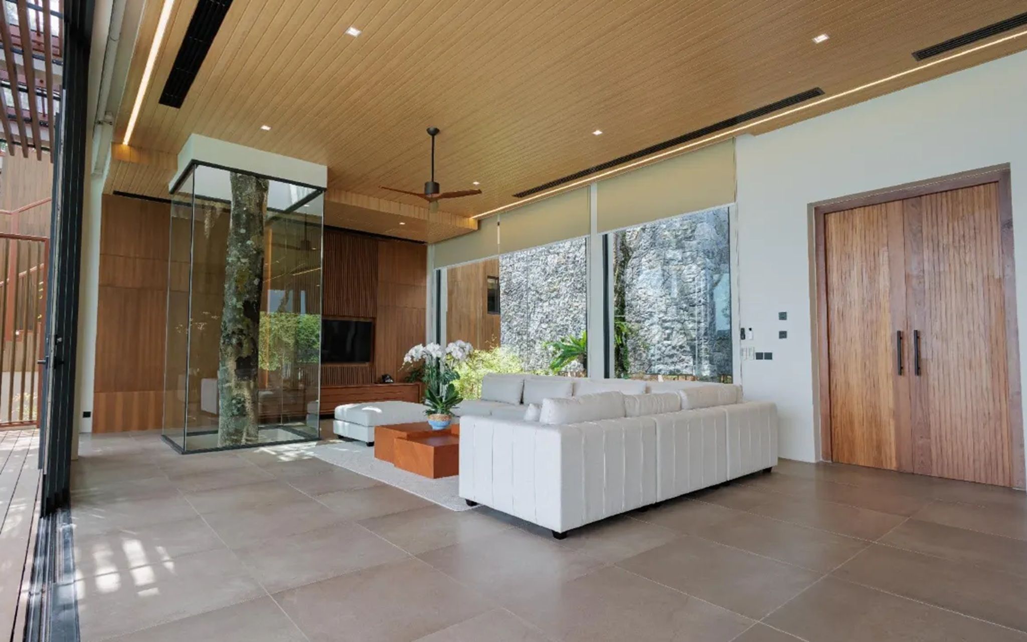 A modern living room with a large sofa, a glass partition, and a wooden ceiling.