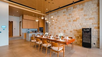 A modern dining area with a long wooden table, cushioned chairs, hanging spherical light fixtures, and a stone wall backdrop.