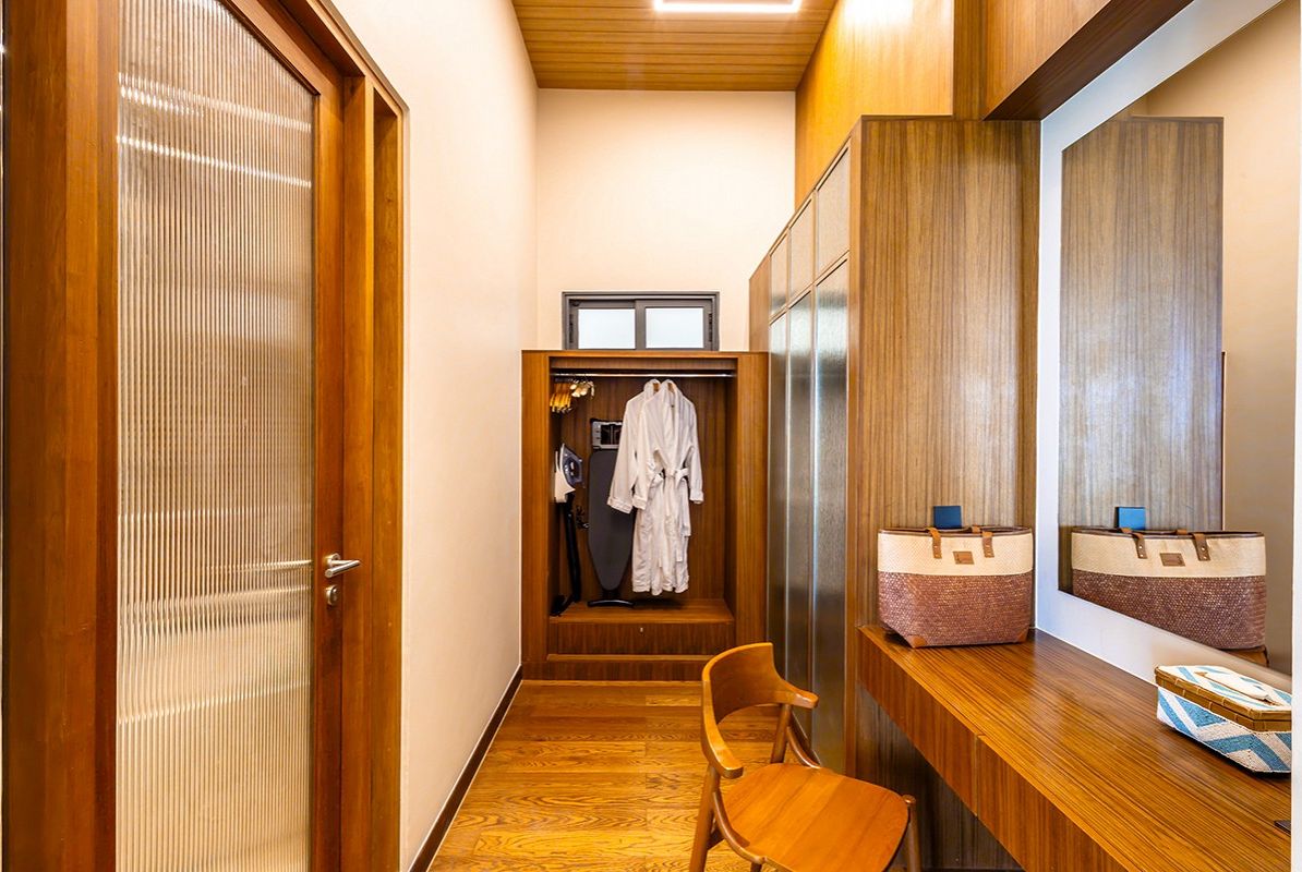 Un pasillo con suelo de madera, una puerta de madera, un espejo y un banco de madera.