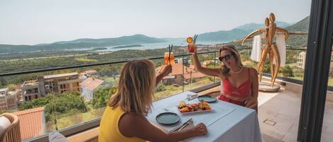 Two people toasting at a table with a scenic view of mountains and a lake.