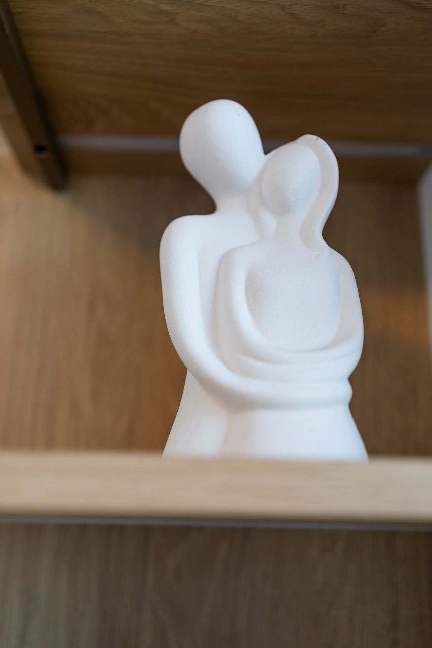A white sculpture of a figure holding a smaller figure on a shelf.