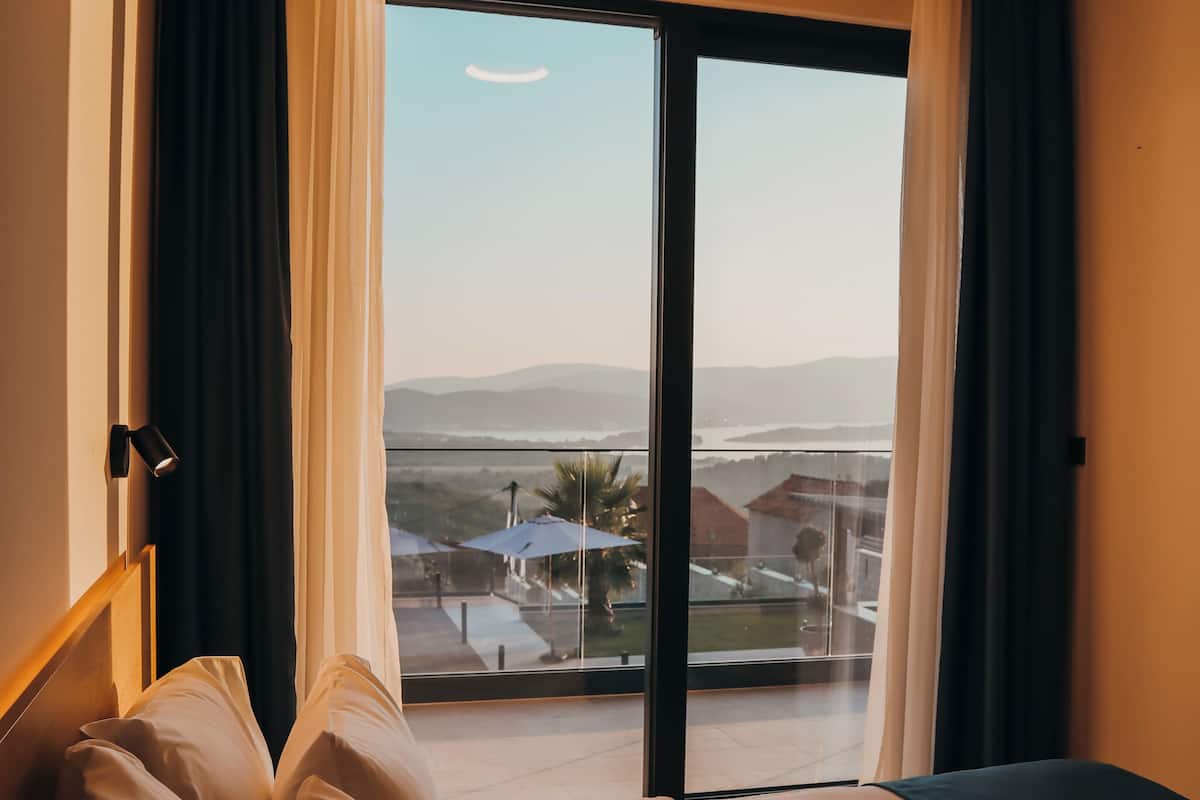 Una habitación de hotel con cama, ventana con cortinas, vistas al paisaje y un equipo de aire acondicionado.
