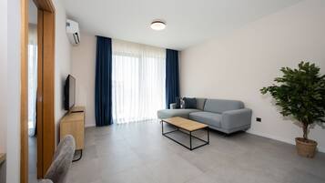 Uma sala de estar moderna com um sofá, uma mesa de centro, uma TV em um móvel e um vaso de planta.