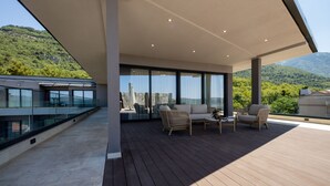 Una terraza moderna al aire libre con barandillas de cristal, suelo de madera y mobiliario.