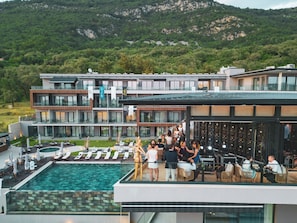 A modern hotel with a rooftop pool, outdoor seating, and a view of a mountainous landscape.