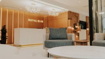 A modern hotel lobby with a reception desk labeled 'ROYAL BLUE,' comfortable seating, and a minimalist design.