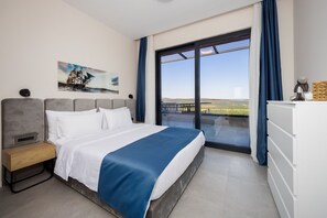 Un dormitorio con cama, mesita de noche, cómoda, un cuadro y un ventanal con vistas.