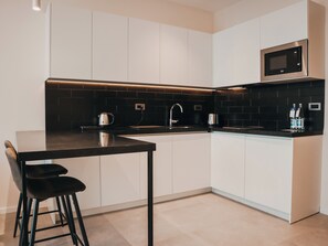 A modern kitchen with a black countertop, white cabinets, a stainless steel microwave, and a coffee maker. - Royal Blue Resort And Residences (Kotor)