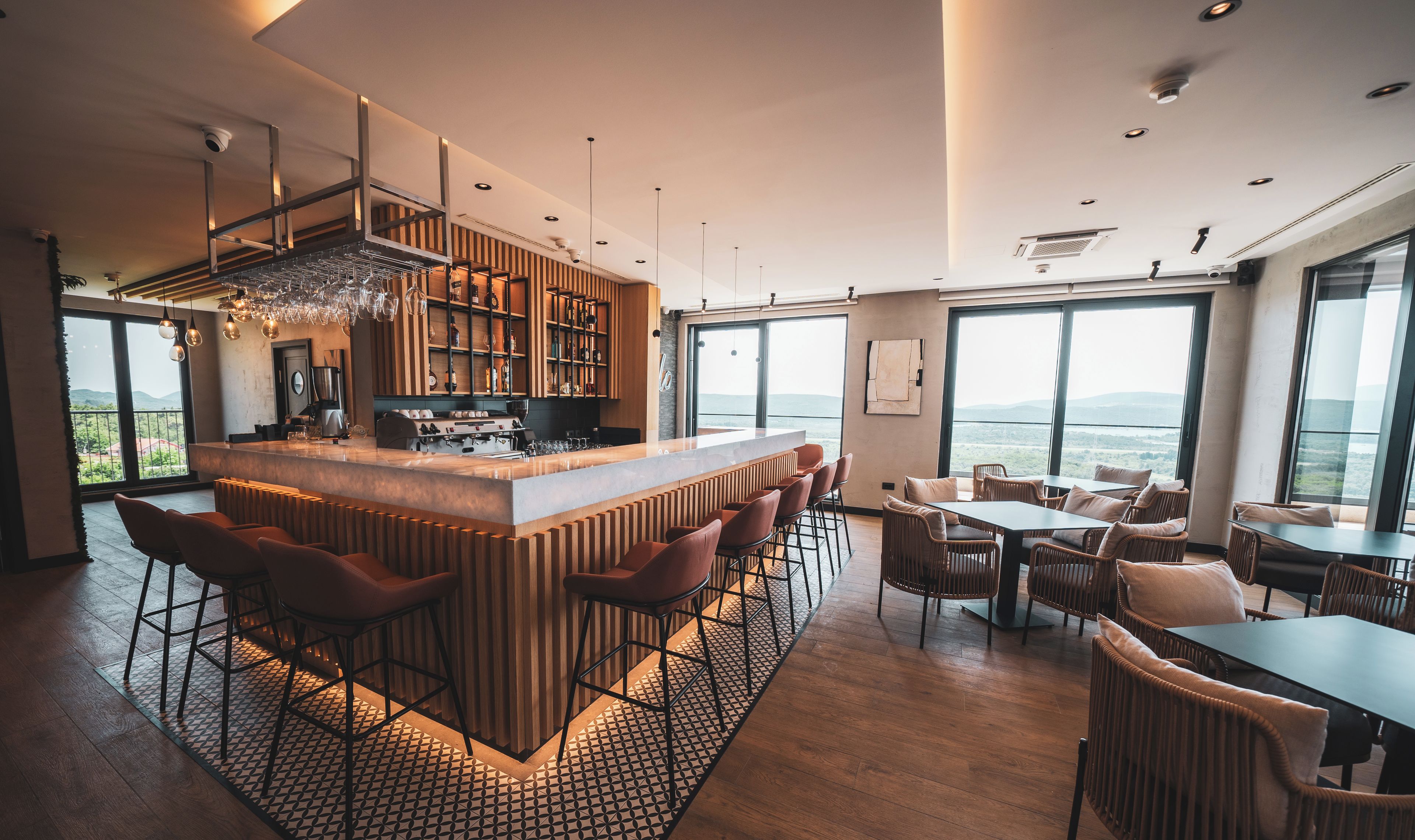 Uma área de bar moderna com ilha central, banquetas e vista para o exterior.