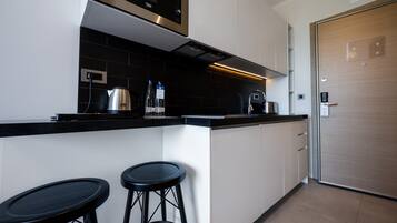 A modern kitchen with a built-in microwave, a kettle, and two bar stools.